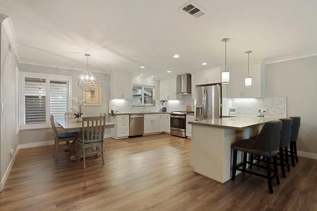 a kitchen with stainless steel appliances granite countertop a stove top oven a sink a dining table and chairs with wooden floor