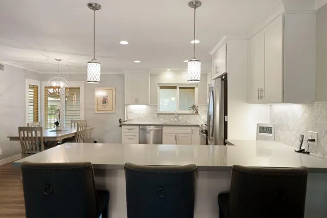 a kitchen with stainless steel appliances granite countertop a sink a stove a refrigerator and chairs