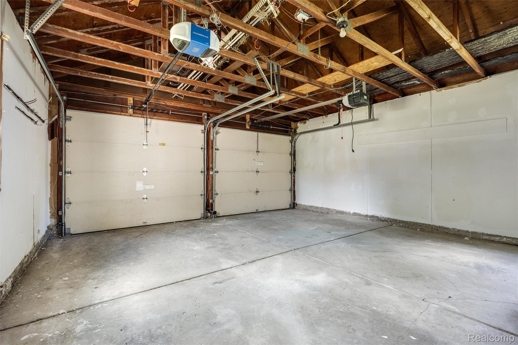 4942 Butler Drive Troy, MI 48085 - Photo 23 of 33 Spacious garage featuring two overhead doors with openers, exposed wood beam ceiling, and concrete flooring