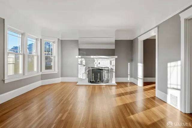 a view of an empty room with wooden floor fireplace and a window