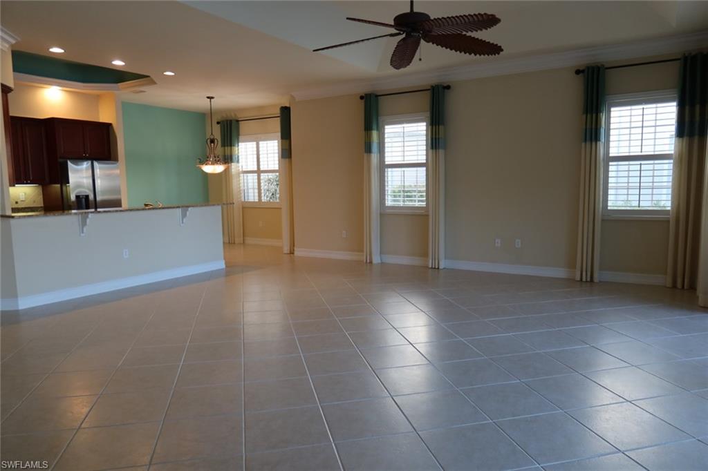 7168 Lemuria Circle, Unit 1701 Naples, FL 34109 - Photo 3 of 39 Expansive open-concept living space featuring neutral tile flooring, a tray ceiling with a ceiling fan, and two windows with plantation shutters
