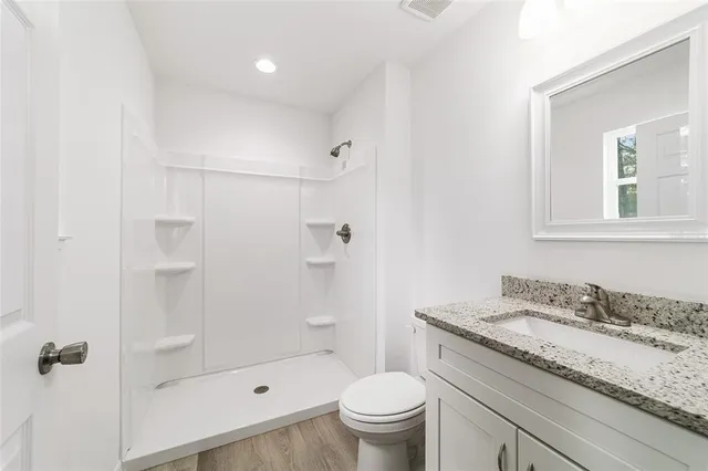 a bathroom with a granite countertop sink a toilet and shower