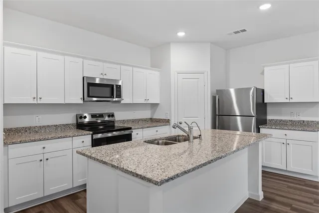 a view of a kitchen with a refrigerator a kitchen island a stove and white cabinets with wooden floor