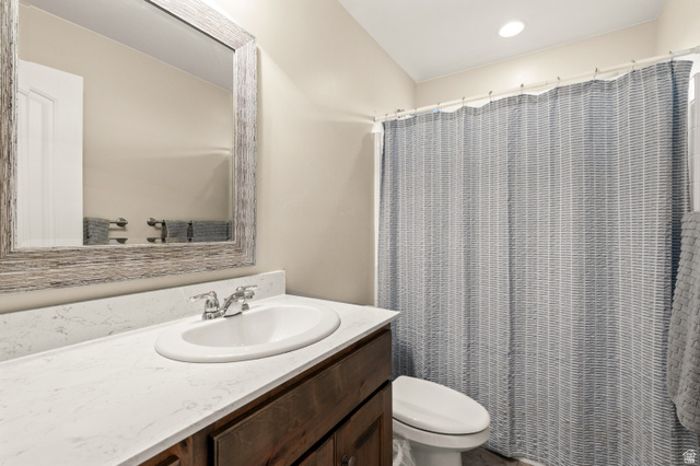 1145 North Christley Lane, Unit 48 Elk Ridge, UT 84651 - Photo 22 of 38 Bathroom featuring a wood-finish vanity with an integrated sink and light-toned countertop, a decorative mirror with a distressed frame, a toilet, and a shower area