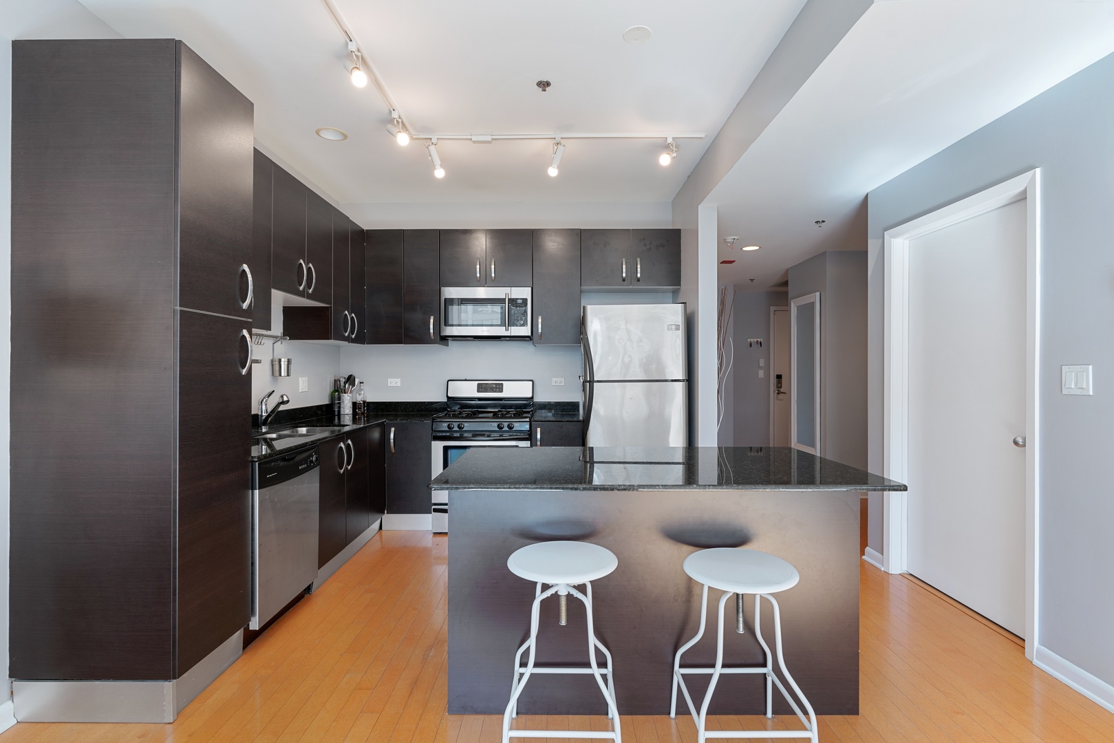 225 South Sangamon Street, Unit 402 Chicago, IL 60607 - Photo 6 of 12 a kitchen with stainless steel appliances kitchen island granite countertop a refrigerator a stove a sink a dining table and chairs with wooden floor