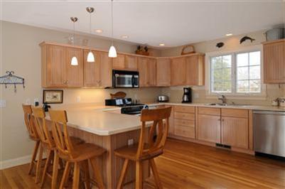 127 West Bay Road, Unit A Osterville, MA 02655 - Photo 8 of 11 a kitchen with kitchen island granite countertop wooden floors and white cabinets