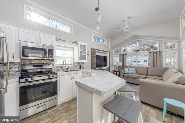 a living room with stainless steel appliances granite countertop a stove top oven a sink dishwasher a dining table and chairs with wooden floor