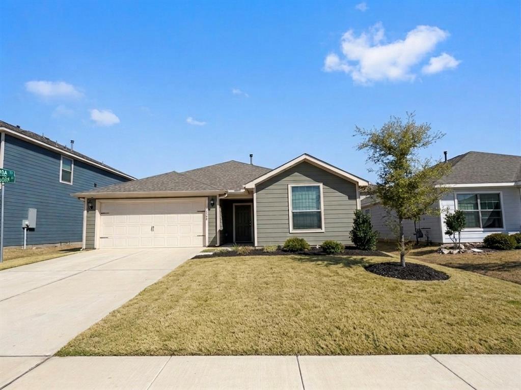 Ranch-style house with an attached garage, a front yard, concrete driveway, and a shingled roof
