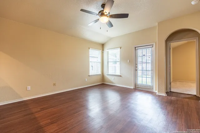 an empty room with wooden floor chandelier fan and windows
