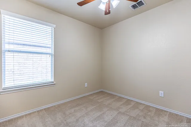 an empty room with a chandelier fan and windows