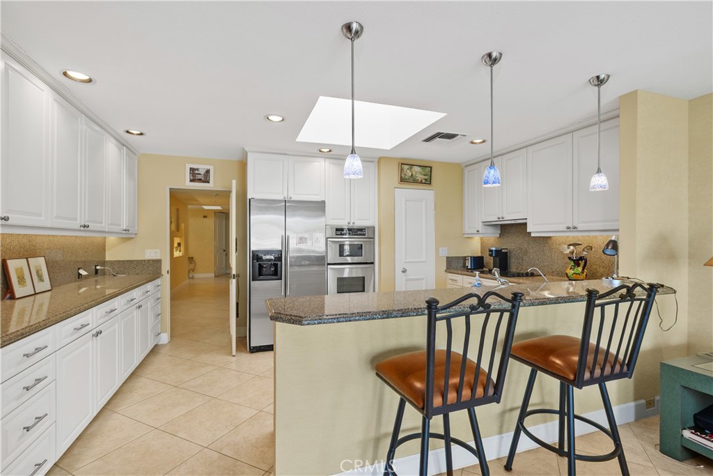 5 Princeton Drive Rancho Mirage, CA 92270 - Photo 12 of 27 a kitchen with stainless steel appliances kitchen island granite countertop a dining table chairs and white cabinets