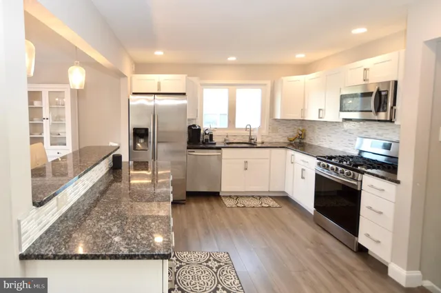 a kitchen with stainless steel appliances granite countertop a stove top oven a sink dishwasher a refrigerator and white cabinets with wooden floor