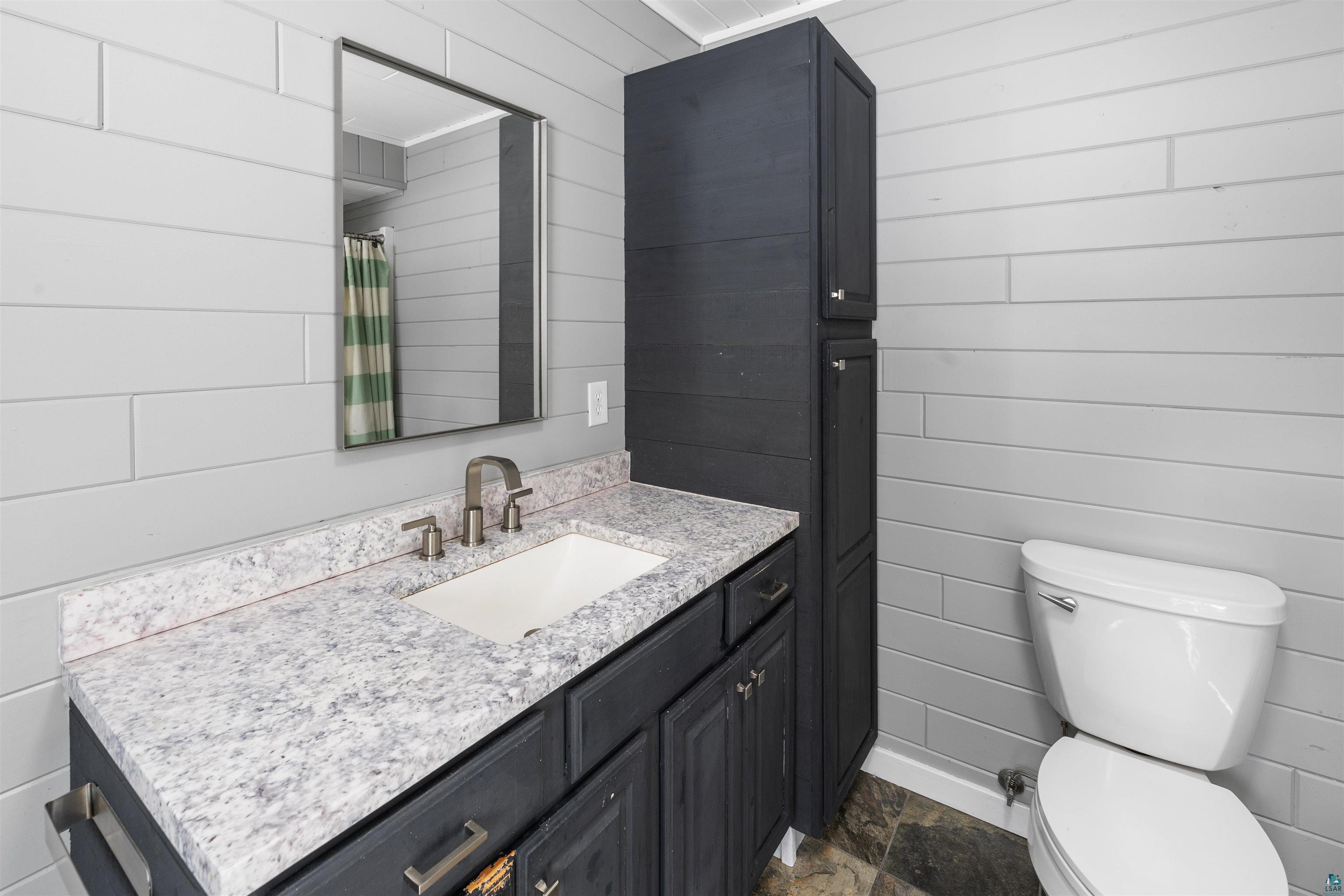 13462 Villa Road Ely, MN 55731 - Photo 21 of 68 Primary bathroom featuring vanity, wood walls, dark stone finish flooring, and a shower with shower curtain