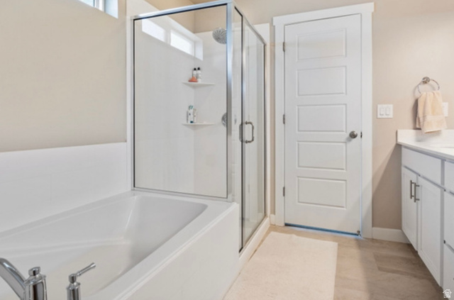1295 East Granite Peak Road Eagle Mountain, UT 84005 - Photo 19 of 35 Modern bathroom featuring a built-in tub, a glass-enclosed shower, a vanity with a white countertop and base cabinetry, and light-colored flooring