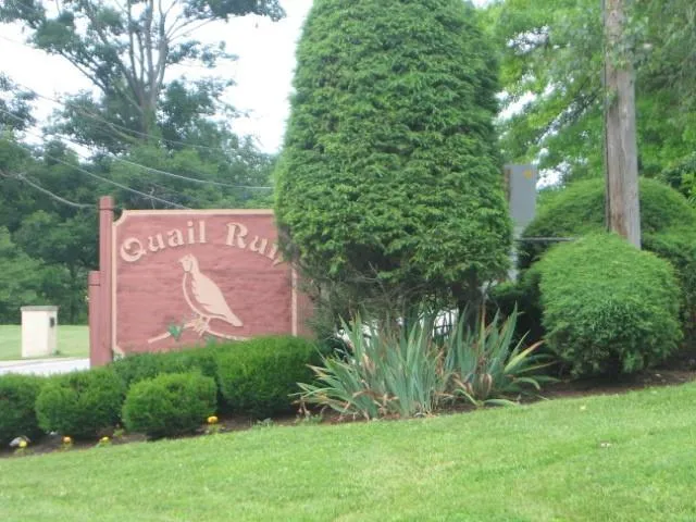 a sign that is sitting in front of a big yard with plants and large trees