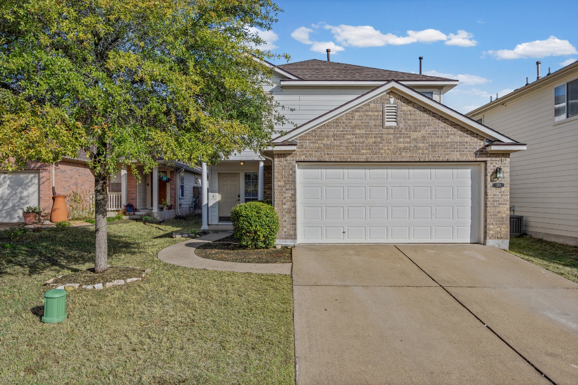 Traditional home featuring driveway, an attached garage, brick siding, and a front yard