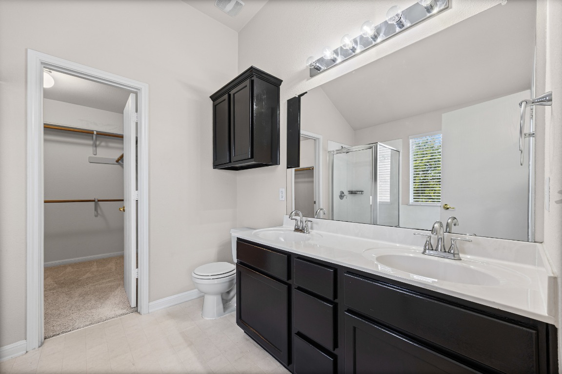 336 Celery Loop Austin, TX 78748 - Photo 18 of 32 Bathroom featuring a spacious closet, double vanity, a stall shower, lofted ceiling, and light floors