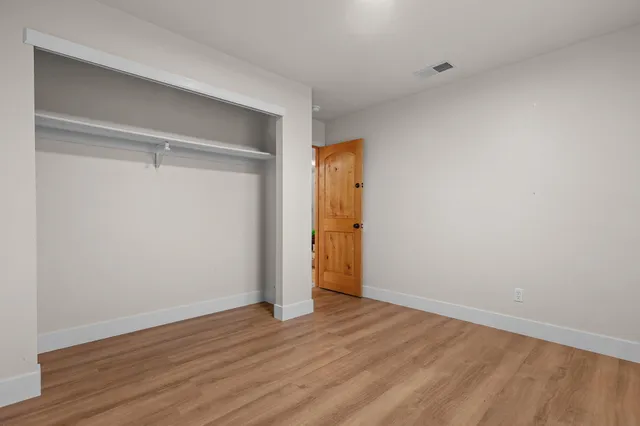 a view of an empty room with wooden floor and closet