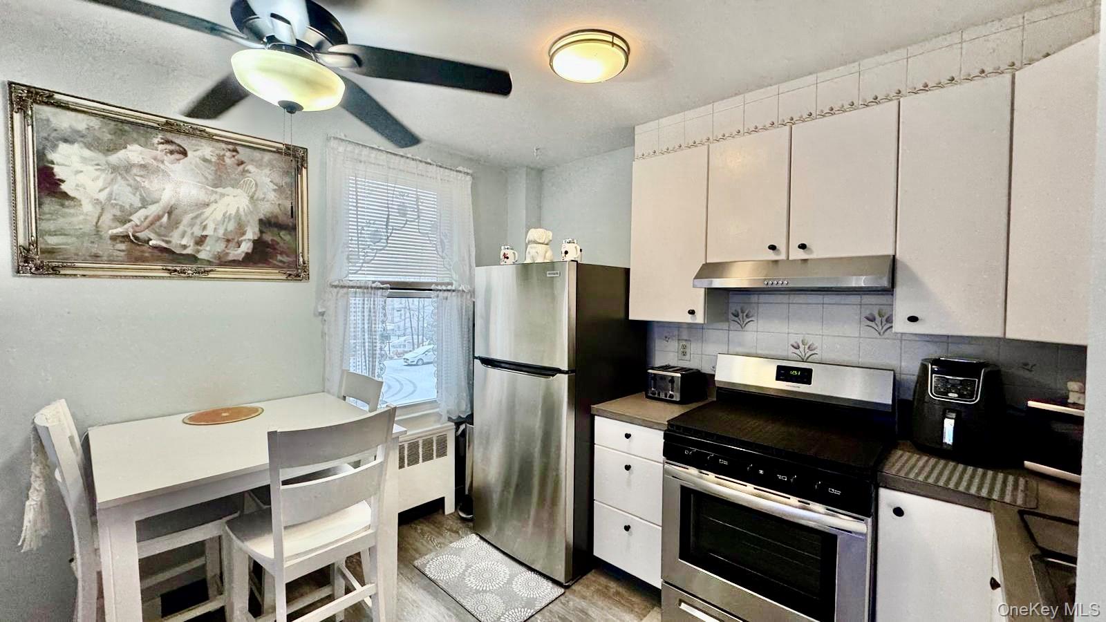 25 Trinity Place, Unit 2K New Rochelle, NY 10805 - Photo 7 of 25 The kitchen features white cabinetry, a stainless steel refrigerator, an oven with a range hood, and a ceiling fan with integrated lighting