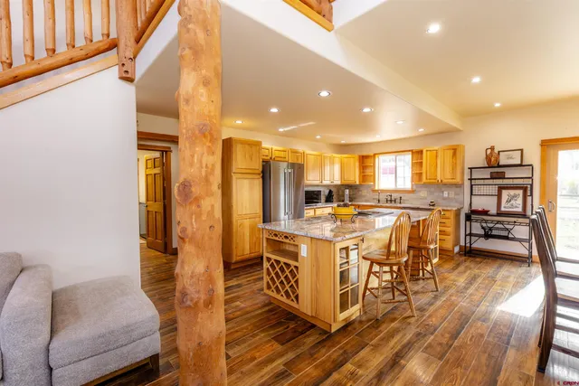 a open kitchen with stainless steel appliances kitchen island granite countertop a refrigerator a stove a dining table and chairs with wooden floor