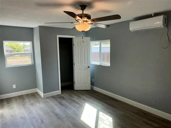 an empty room with wooden floor chandelier fan and windows