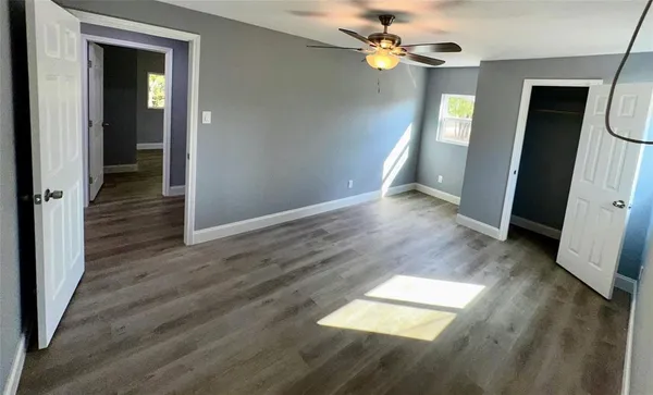 an empty room with wooden floor a ceiling fan and windows