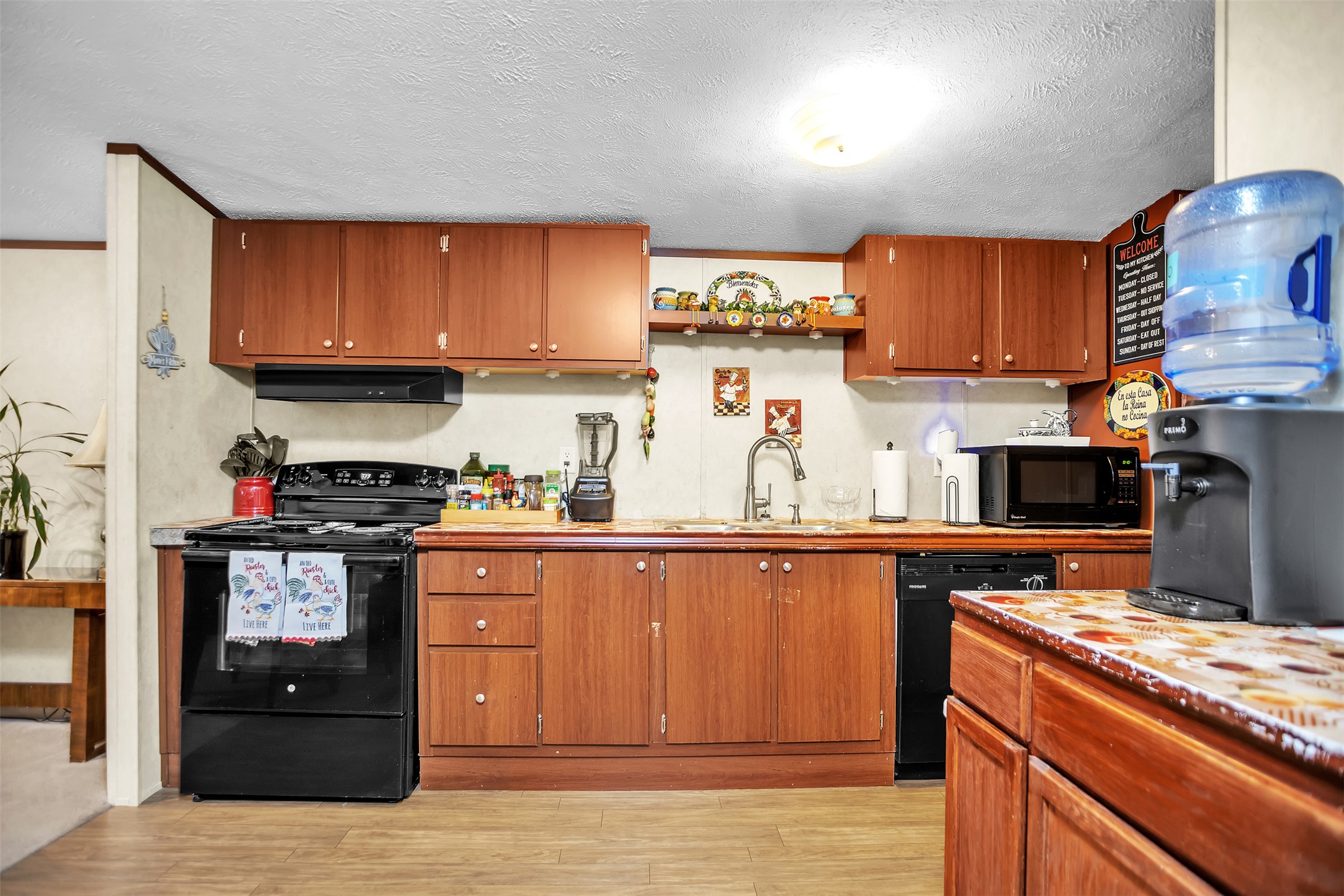 363 El Rey Drive Kyle, TX 78640 - Photo 11 of 40 Kitchen featuring black appliances, open shelves, light wood-style flooring, wood finish cabinets, and a textured ceiling