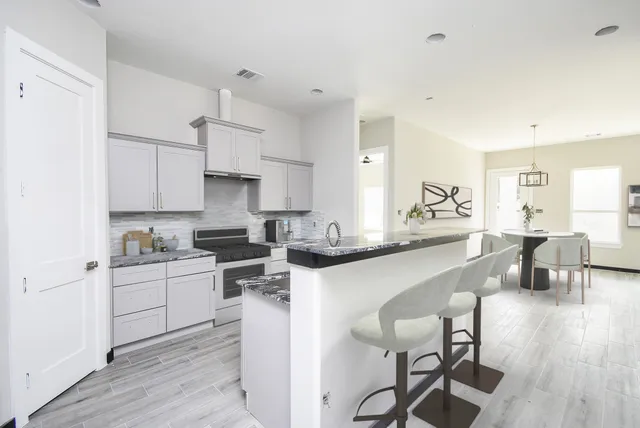 a kitchen with stainless steel appliances white cabinets a sink a stove a dining table and chairs