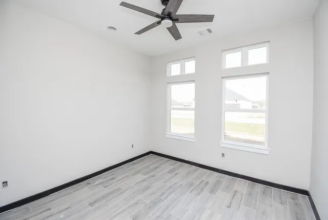 an empty room with wooden floor windows and fan