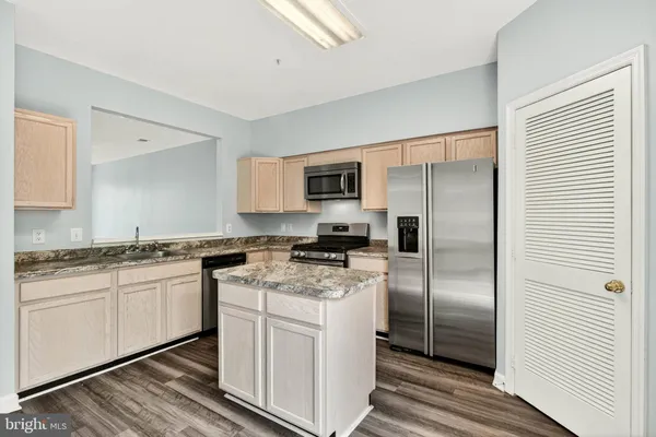 a kitchen with stainless steel appliances granite countertop a refrigerator a stove a sink and white cabinets with wooden floor
