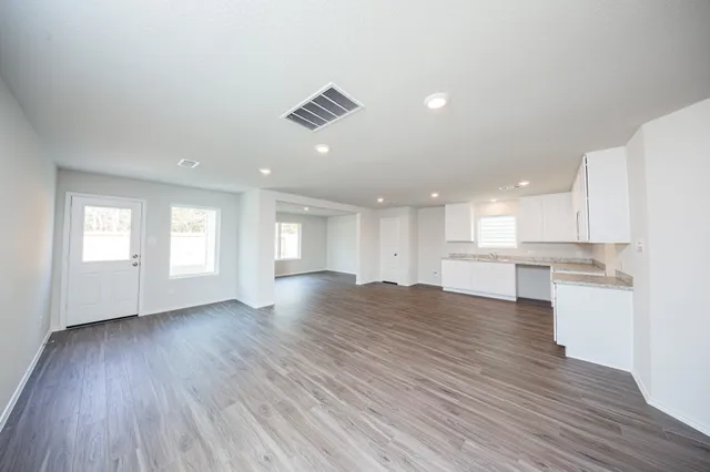 a view of an empty room with wooden floor and a kitchen