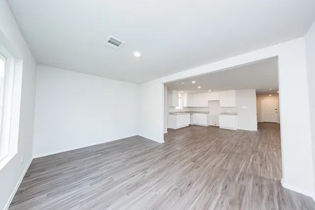 a view of empty room with wooden floor and kitchen windows