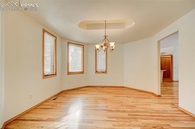 15091 Ridgefield Lane Colorado Springs, CO 80921 - Photo 10 of 35 Spare room featuring a tray ceiling, a chandelier, and light hardwood / wood-style flooring