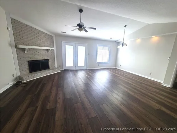 a view of an empty room with wooden floor fireplace and a window