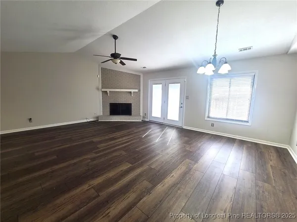 a view of an empty room with wooden floor fireplace and a window