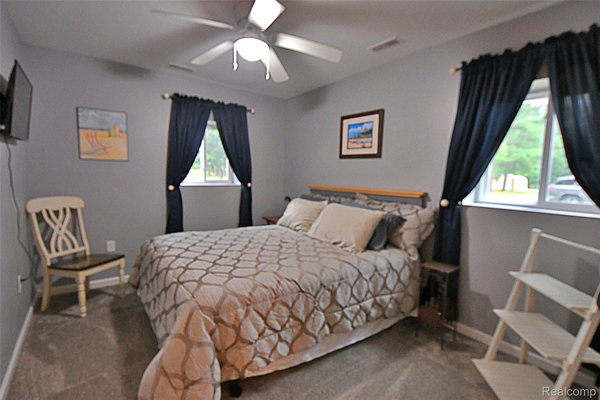 9611 Monroe Road St. Helen, MI 48656 - Photo 17 of 24 Carpeted room featuring a ceiling fan with integrated lighting, two windows with dark curtains, and light gray wall paint