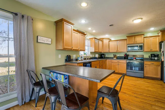 a kitchen with stainless steel appliances granite countertop a stove top oven a sink a dining table and chairs with wooden floor