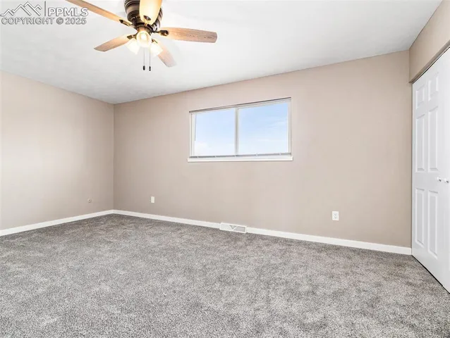 an empty room with a chandelier fan and windows