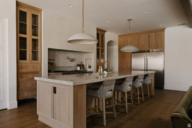 2281 South Crimson Cliffs Way St. George, UT 84790 - Photo 13 of 47 Kitchen featuring glass insert cabinets, stainless steel built in refrigerator, backsplash, dark wood-type flooring, and a large island with sink