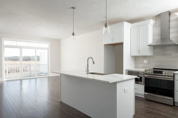 a kitchen with stainless steel appliances granite countertop a stove a sink a refrigerator and white cabinets with wooden floor