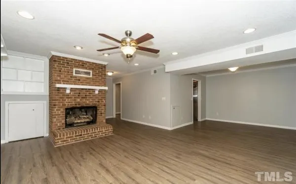 an empty room with wooden floor fireplace and windows