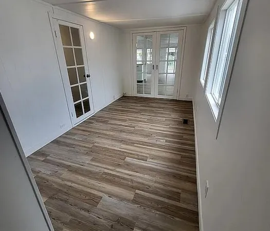 an empty room with wooden floor chandelier fan and windows