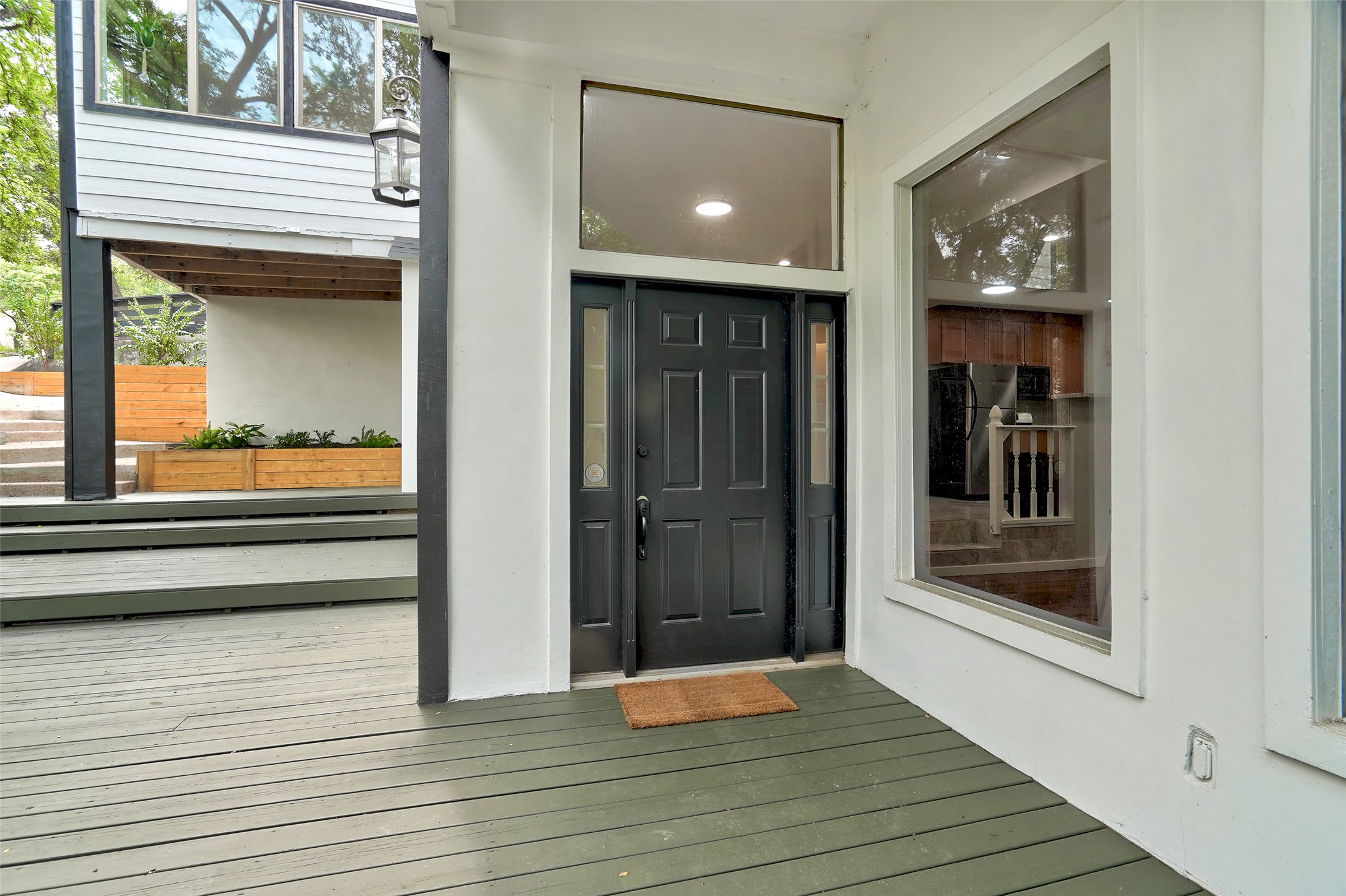 A welcoming entry invites guests onto a spacious wooden deck with planters and outdoor lighting.