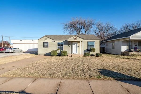 a front view of a house with a dirt yard and a large tree