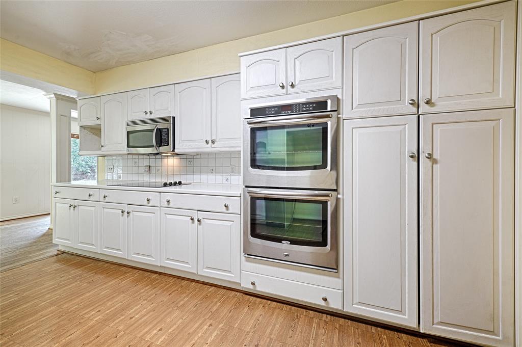 3004 Wingren Road Irving, TX 75062 - Photo 6 of 18 White cabinetry, wood-finish flooring, stainless steel double ovens, stainless steel microwave, and a white tile backsplash