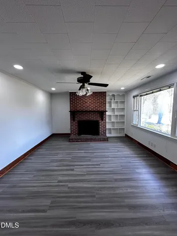 an empty room with wooden floor fireplace and windows