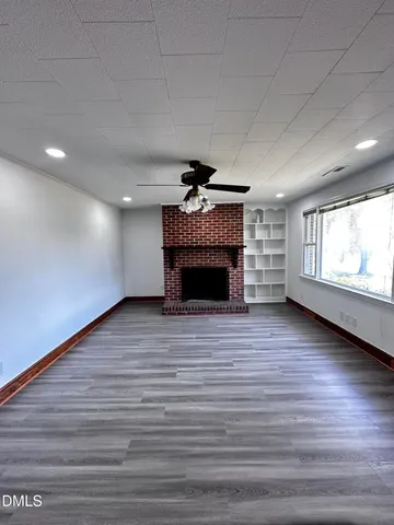 an empty room with wooden floor fireplace and windows