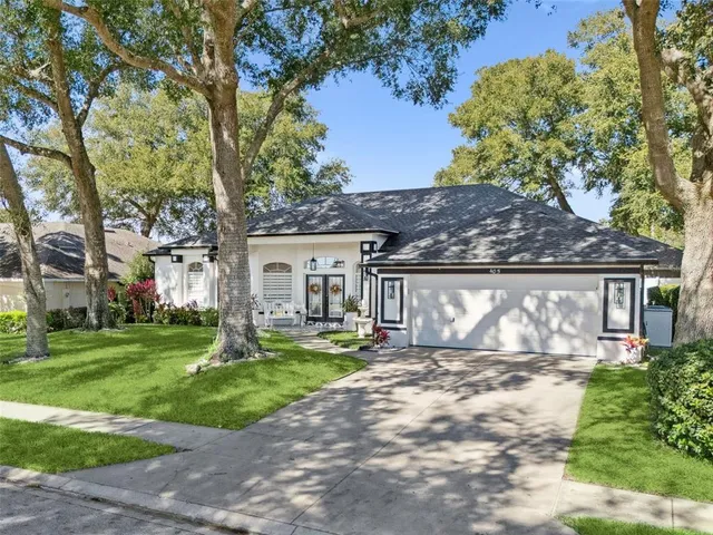 a view of a white house next to a yard with big trees