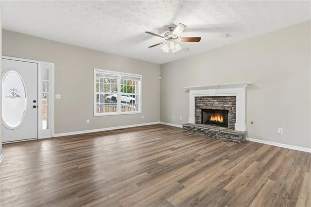 a view of an empty room with wooden floor fireplace and a window