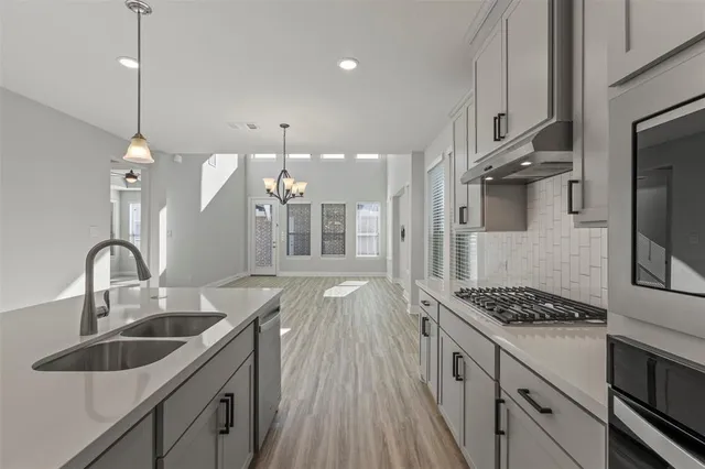 a kitchen with stainless steel appliances a sink a stove a refrigerator and white cabinets with wooden floor